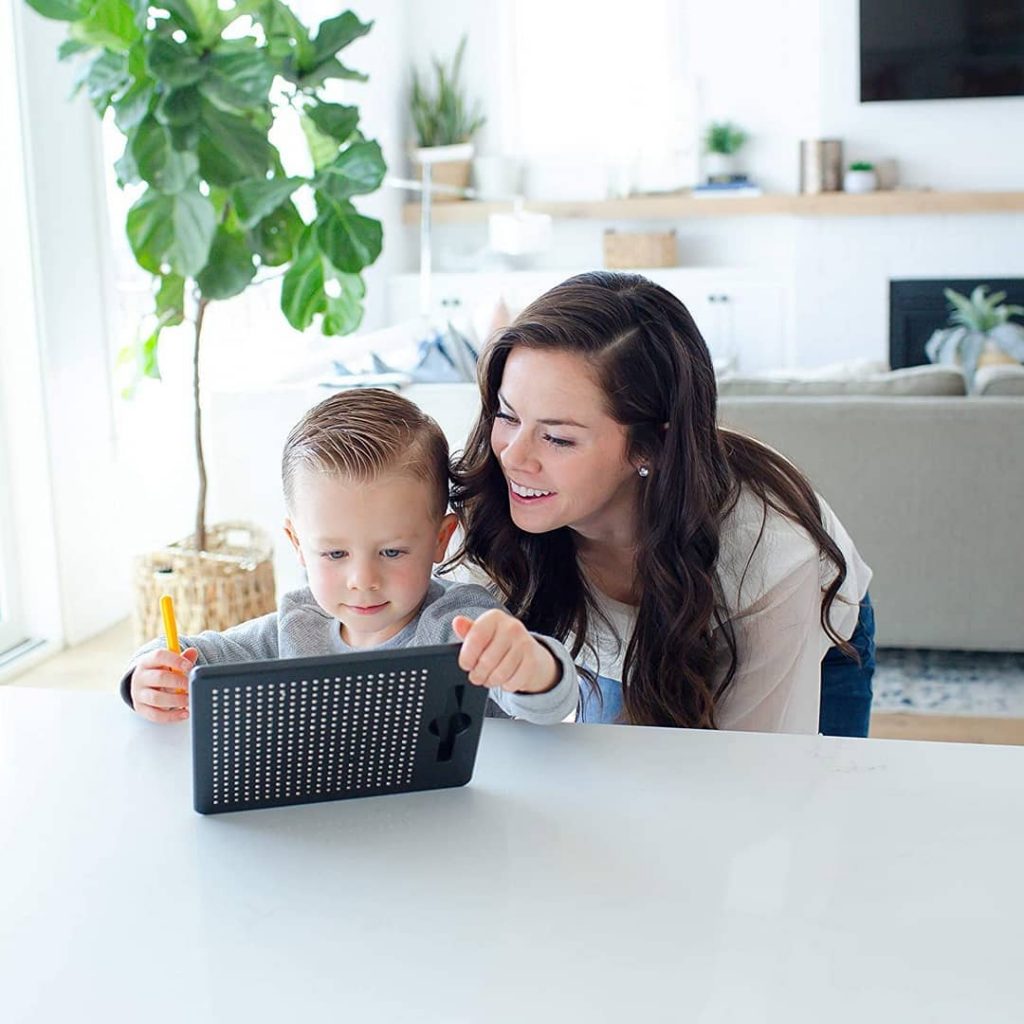 criança brinca com lousa mágica enquanto sua mãe supervisiona.