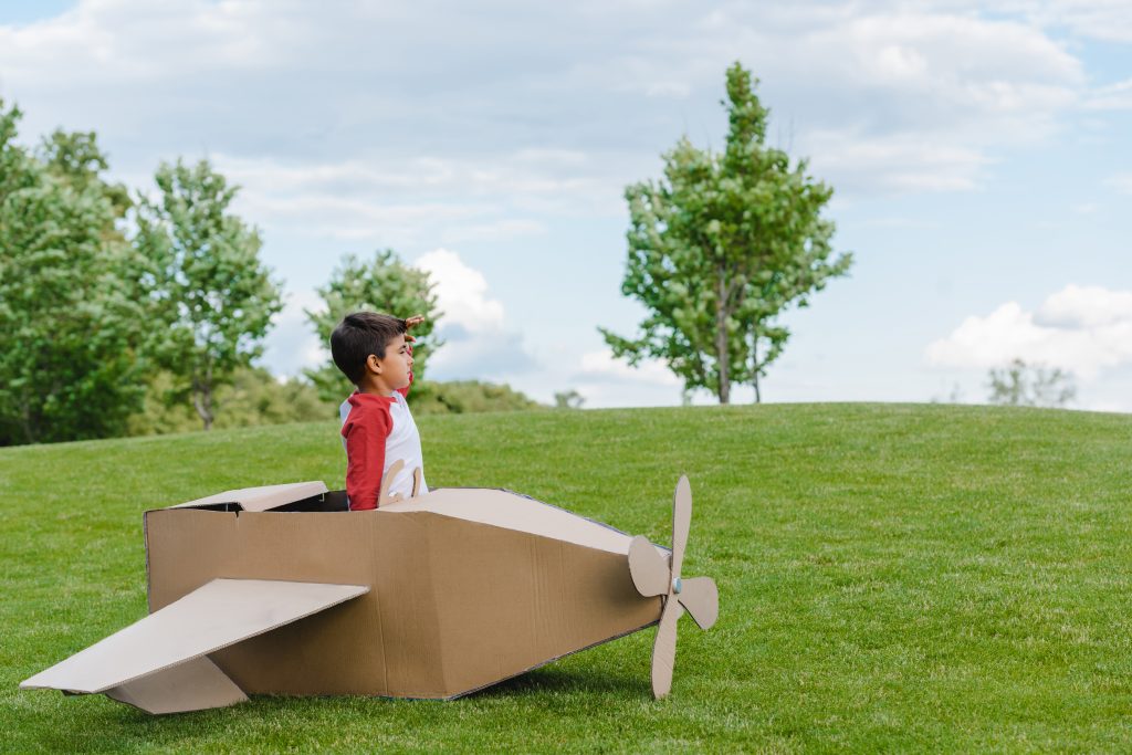 Menino sentado no avião de brinquedo de papelão e brincando no parque